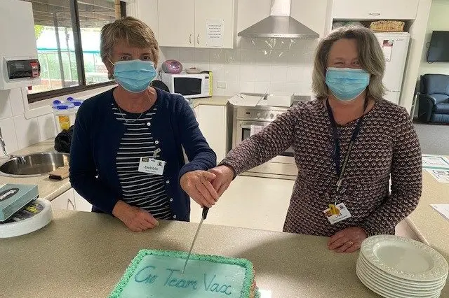 CELEBRATED: BHS vaccination ambassador and project officer Debra Cullen (left) with clinical services director Lisa Allen ready to cut the celebration cake with the vax team and share with people jabbed on the day.