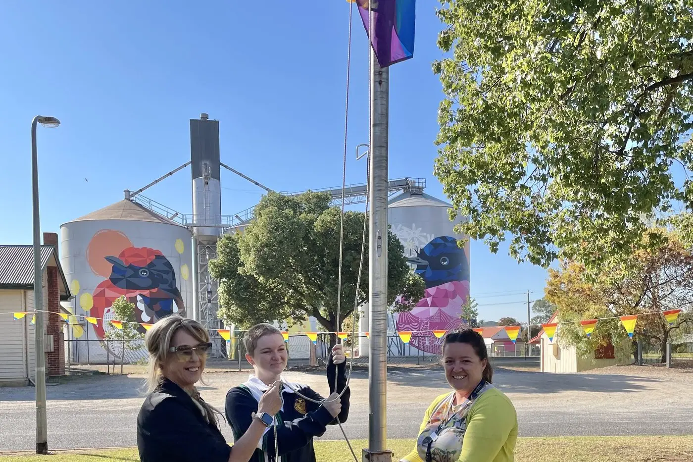 UNDER THE FLAG WE STAND: Nikki James (left), Finn Welsh and Sophie Price raise the rainbow flag at a community gathering event for IDAHOBIT last Wednesday.